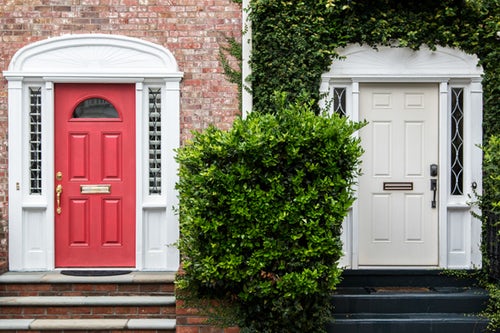 2 halves of the same house look completely different. One half has a white door surrounded by dark green ivy. The other half has a dark pink door surrounded by pink brick. Both homes have curb appeal. 